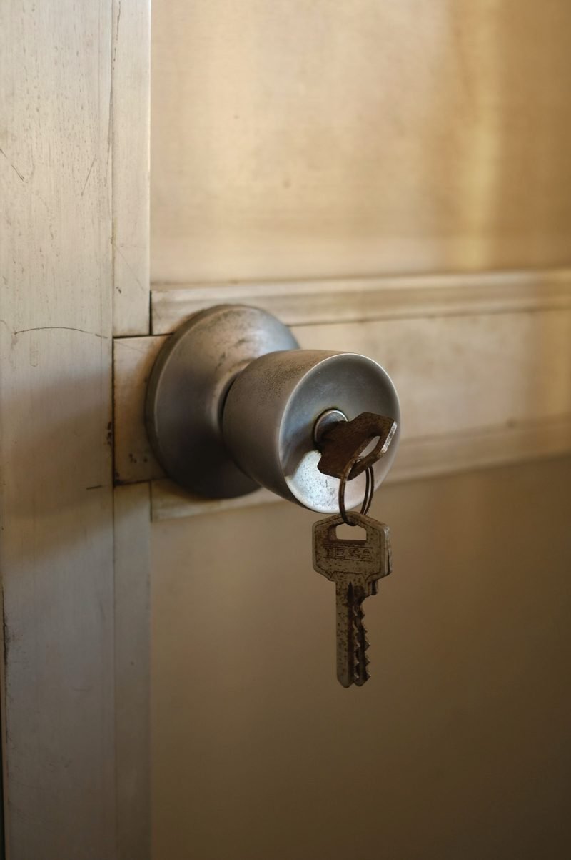 A key with a small ring hanging from a brushed metal door knob