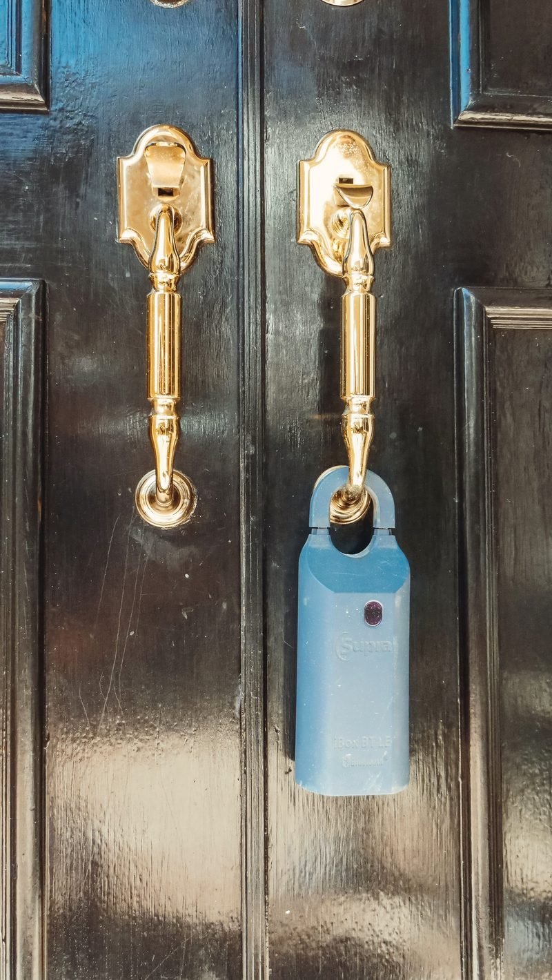 A blue real estate lockbox hanging from the brass handle of a black front door