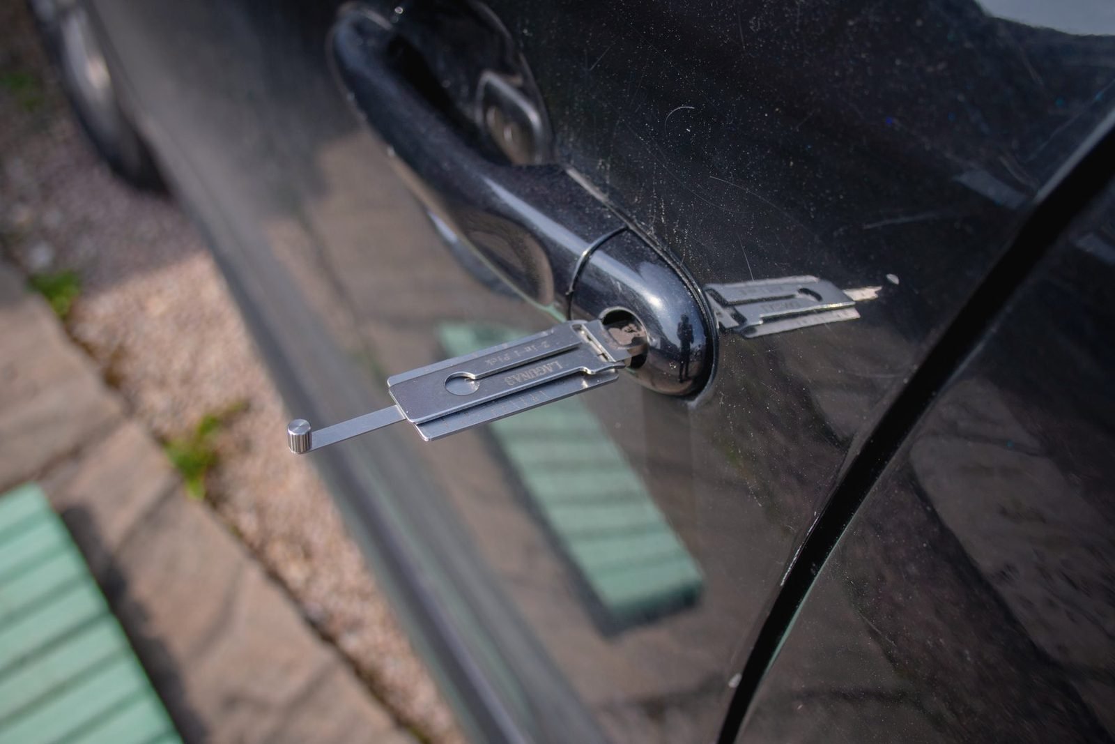 A flat locksmith tool inserted into the door lock of a dark car
