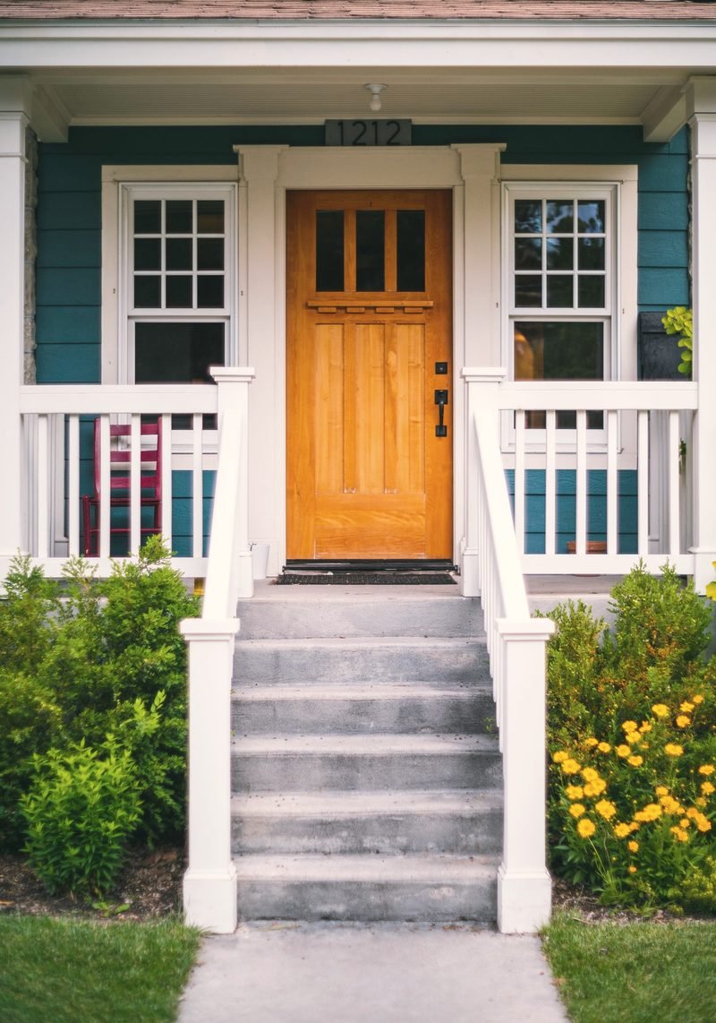 A wooden front door at the top of white porch steps with flowers either side