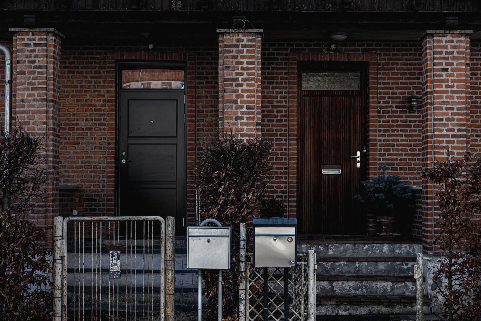 Two entry doors in a red brick building with metal gates and mailboxes in front