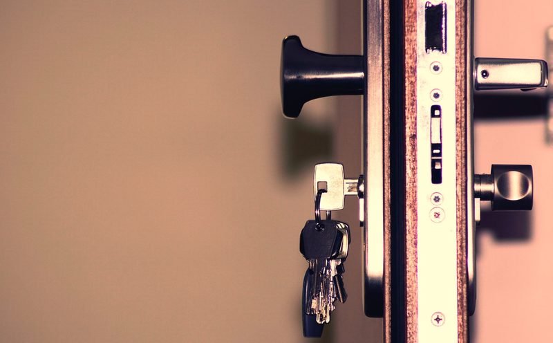 The edge of an open door showing a mortise lock body, keys hanging in the cylinder